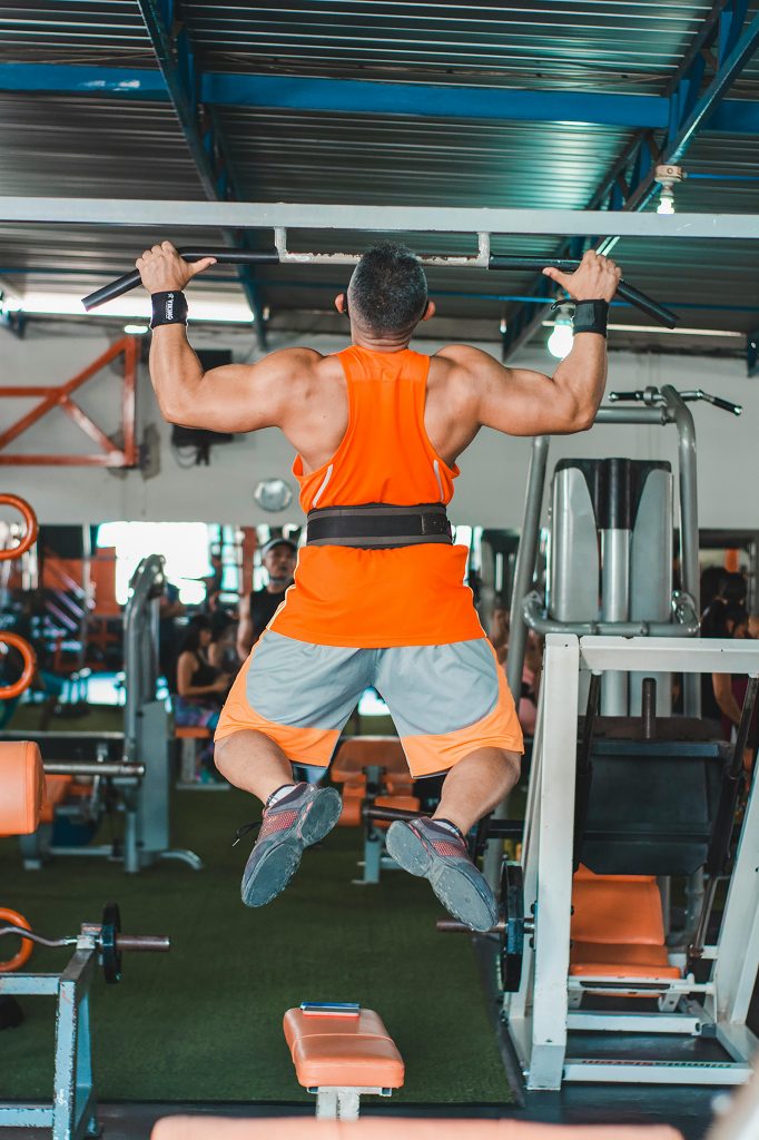 Muscular man in bright activewear doing pull ups in a gym setting.